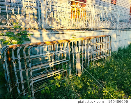 Rusty metal fencing against sunlit wall with vibrant greenery 140406696
