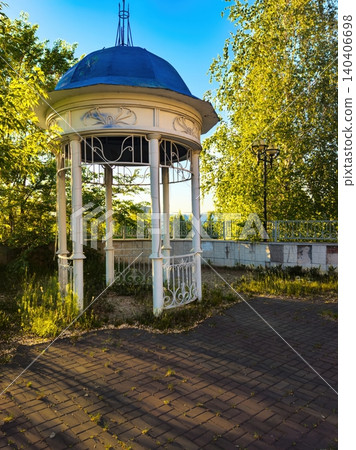 Tranquil white gazebo in lush green park with pathway and blue sky backdrop Tranquil white gazebo in lush green park with pathway and blue sky backdrop 140406698
