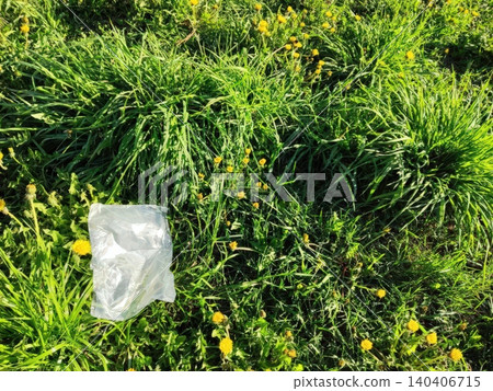 Plastic bag littering green grass with yellow dandelions in a sunny field Plastic bag littering green grass with yellow dandelions in a sunny field 140406715
