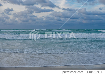 Waves crash on the shore under a cloudy sky at twilight on a beach 140406911