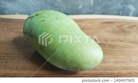 Single raw organic green mango placed on a wood surface. Single raw organic green mango placed on a wood surface. 140407005