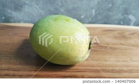 Single raw organic green mango placed on a wood surface. Single raw organic green mango placed on a wood surface. 140407006