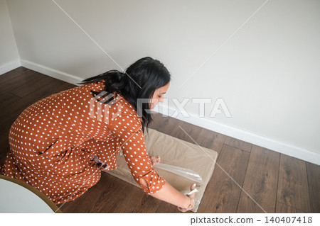 A woman in a polka dot dress is cutting a piece of plastic wrap 140407418