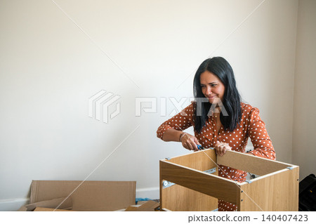 A woman is working on assembling a piece of furniture A woman is working on assembling a piece of furniture 140407423
