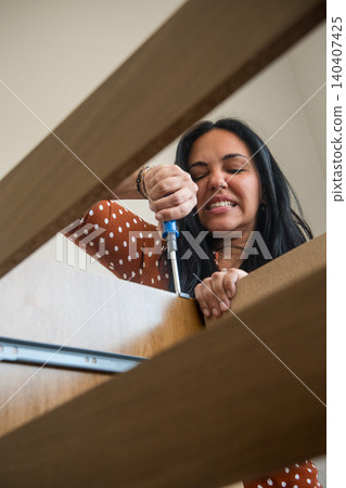 A woman is using a screwdriver to fix a piece of furniture 140407425