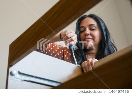 A woman is fixing a cabinet with a screwdriver A woman is fixing a cabinet with a screwdriver 140407426