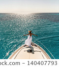 Young woman in white dress standing on yacht bow over turquoise sea 140407793