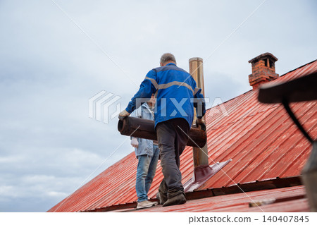 Roofer repairing metal chimney on house roof. Construction worker replacing pipe on exterior of building. Maintenance service, installation of ventilation system and building renovation. Roofer repairing metal chimney on house roof. Construction worker replacing pipe on exterior of building. Maintenance service, installation of ventilation system and building renovation. 140407845