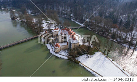 Picturesque drone panorama shows historic Otocec Castle covered in light snow. Frozen park trees, wooden bridges, and cold green Krka river frame medieval island palace in winter time. Picturesque drone panorama shows historic Otocec Castle covered in light snow. Frozen park trees, wooden bridges, and cold green Krka river frame medieval island palace in winter time. 140408318