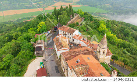 Famous medieval fortress town of Motovun stands proud on green hill in Istria. Aerial perspective shows ancient city walls, terracotta roofs, and mist rising from surrounding truffle forests. Famous medieval fortress town of Motovun stands proud on green hill in Istria. Aerial perspective shows ancient city walls, terracotta roofs, and mist rising from surrounding truffle forests. 140408331