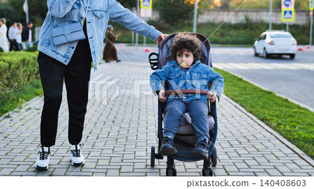 Mother pushing child in stroller on city street, enjoying family walk outdoors Mother pushing child in stroller on city street, enjoying family walk outdoors 140408603