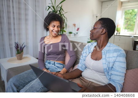 Mother and daughter looking at each other while using laptop on sofa at home 140408608