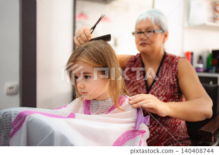 Hairdresser giving little girl haircut in beauty salon Hairdresser giving little girl haircut in beauty salon 140408744