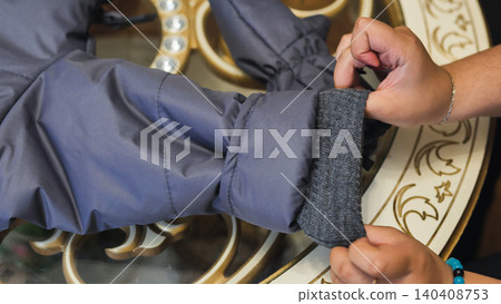 Person hand adjusting winter jacket sleeve cuff, showing clothing detail and fabric Person hand adjusting winter jacket sleeve cuff, showing clothing detail and fabric 140408753