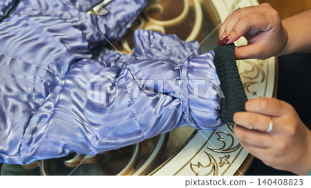 Hands adjusting a purple puffer jacket cuff on a decorative table Hands adjusting a purple puffer jacket cuff on a decorative table 140408823