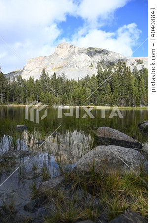 Granite mountain dome reflection on clear alpine lake with foreground boulders. Granite mountain dome reflection on clear alpine lake with foreground boulders. 140408841