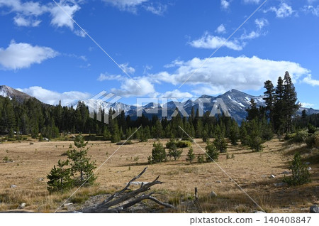 Scenic subalpine lake and pine forest below rugged mountain peaks with white clouds. Scenic subalpine lake and pine forest below rugged mountain peaks with white clouds. 140408847