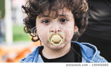 Little boy with curly hair using pacifier, looking at camera 140408860