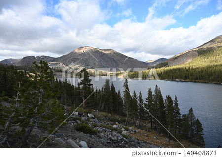 Subalpine mountain lake framed by pine trees under bright fluffy clouds. Subalpine mountain lake framed by pine trees under bright fluffy clouds. 140408871