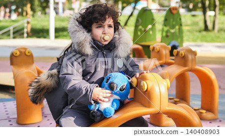 Child on playground ride holding plush toy, pacifier in mouth Child on playground ride holding plush toy, pacifier in mouth 140408903