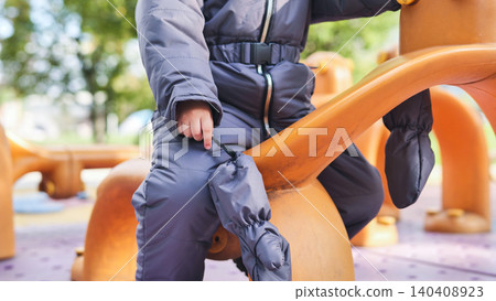 Young child wearing winter overalls playing on a bright playground toy outdoors Young child wearing winter overalls playing on a bright playground toy outdoors 140408923
