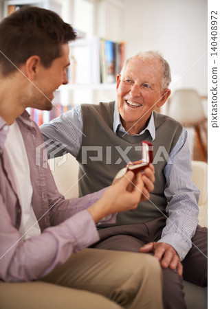 Dad, adult son and medal for present support and congratulations with celebration and bonding at home. Men in living room, family time with reward or award as gift for happiness and gratitude Dad, adult son and medal for present support and congratulations with celebration and bonding at home. Men in living room, family time with reward or award as gift for happiness and gratitude 140408972