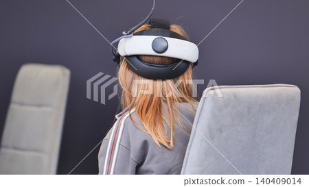 Child wearing a VR headset, sitting in a chair, immersed in a virtual simulation Child wearing a VR headset, sitting in a chair, immersed in a virtual simulation 140409014