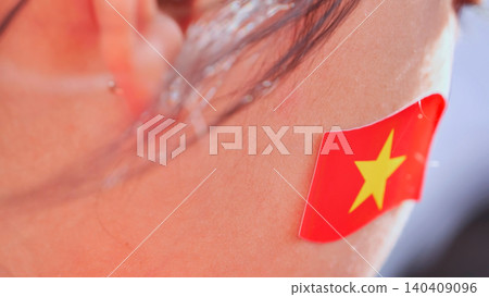 Macro shot of a person's cheek with a Vietnamese flag sticker, showing support and patriotism. Macro shot of a person's cheek with a Vietnamese flag sticker, showing support and patriotism. 140409096