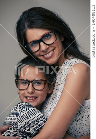 Happy mother, portrait and hugging daughter with love for care or support in fashion on a gray studio background. Mom, child or young kid with smile and glasses in happiness for parenting or bonding Happy mother, portrait and hugging daughter with love for care or support in fashion on a gray studio background. Mom, child or young kid with smile and glasses in happiness for parenting or bonding 140409113