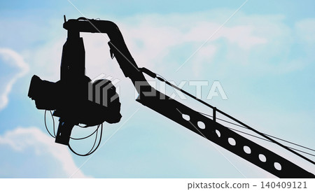 Professional cinema camera on a crane arm, silhouetted against a pale blue sky 140409121
