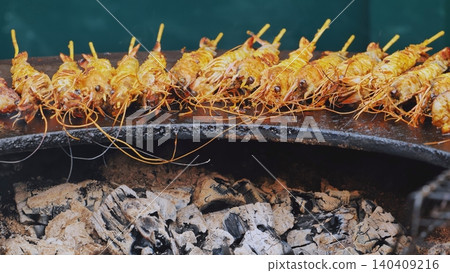 Row of seasoned shrimp skewers grilling over hot charcoal. 140409216