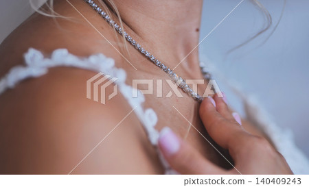 Bride in a white lace dress gently touching her sparkling diamond necklace. Bride in a white lace dress gently touching her sparkling diamond necklace. 140409243