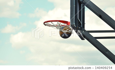 Basketball entering basket against cloudy sky during sports day 140409254
