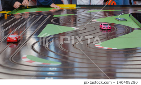 Children playing with a slot car racing set with red and pink toy cars Children playing with a slot car racing set with red and pink toy cars 140409280