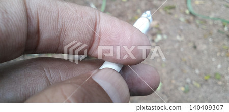 Macro photo showing a person's fingers holding a lit cigarette. Macro photo showing a person's fingers holding a lit cigarette. 140409307