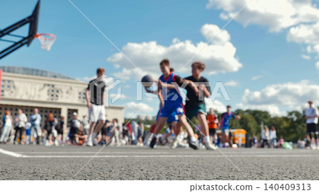 Low angle view of an asphalt basketball court with blurred young players in a streetball game on a sunny day. 140409313