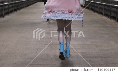 Woman walking on a tiled ground in a pink dress and blue high heel shoes Woman walking on a tiled ground in a pink dress and blue high heel shoes 140409347