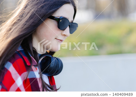 Young stylish woman wearing sunglasses and headphones enjoying music outdoors Young stylish woman wearing sunglasses and headphones enjoying music outdoors 140409489