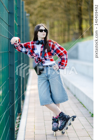 Young woman wearing roller skates posing near a fence in a park 140409492