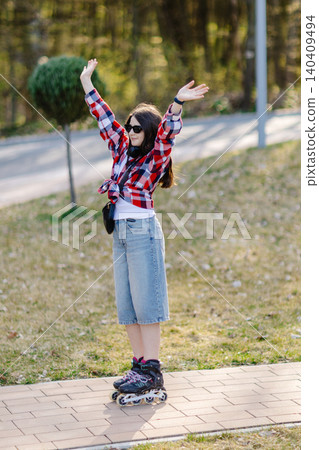 Young woman wearing roller skates raising arms in a park Young woman wearing roller skates raising arms in a park 140409494