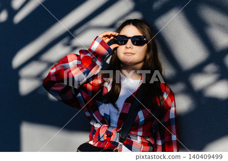 Young student adjusting sunglasses while leaning against wall with shadows Young student adjusting sunglasses while leaning against wall with shadows 140409499