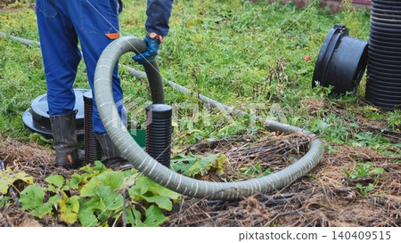 Worker performing septic tank maintenance, pumping waste using a large hose Worker performing septic tank maintenance, pumping waste using a large hose 140409515