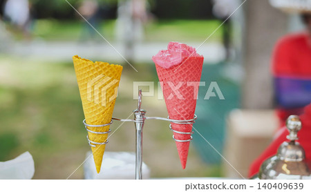 Strawberry sorbet ice cream in a pink waffle cone with an empty yellow cone Strawberry sorbet ice cream in a pink waffle cone with an empty yellow cone 140409639