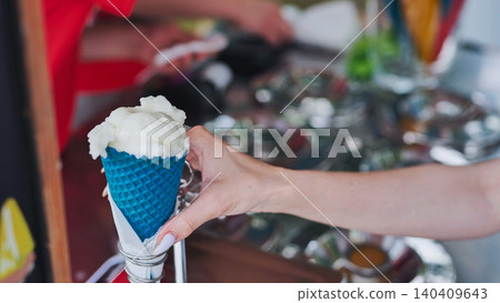 Vendor holding two colorful ice cream cones at a summer fair Vendor holding two colorful ice cream cones at a summer fair 140409643