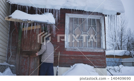 Man entering rustic wooden cabin during cold winter with snow and icicles hanging Man entering rustic wooden cabin during cold winter with snow and icicles hanging 140409690