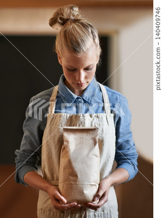 Woman, barista and paper bag with apron in coffee shop, small business owner with parcel and serious for service. Catering, hospitality and entrepreneur with eco friendly package for product in store 140409746