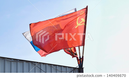 Soviet and Russian flags waving in the wind over a metallic fence 140409870