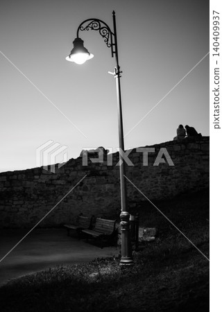 Glowing street lamp by stone wall at dusk Glowing street lamp by stone wall at dusk 140409937