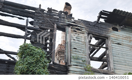 Ruins of a fire-damaged wooden building with charred beams and overgrown vines against a gray sky Ruins of a fire-damaged wooden building with charred beams and overgrown vines against a gray sky 140410051