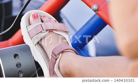 Young girl playing racing simulation game, hands on steering wheel at home. Person's foot in sandals pressing the accelerator pedal while driving a go-kart for fun. Young girl playing racing simulation game, hands on steering wheel at home. Person's foot in sandals pressing the accelerator pedal while driving a go-kart for fun. 140410101